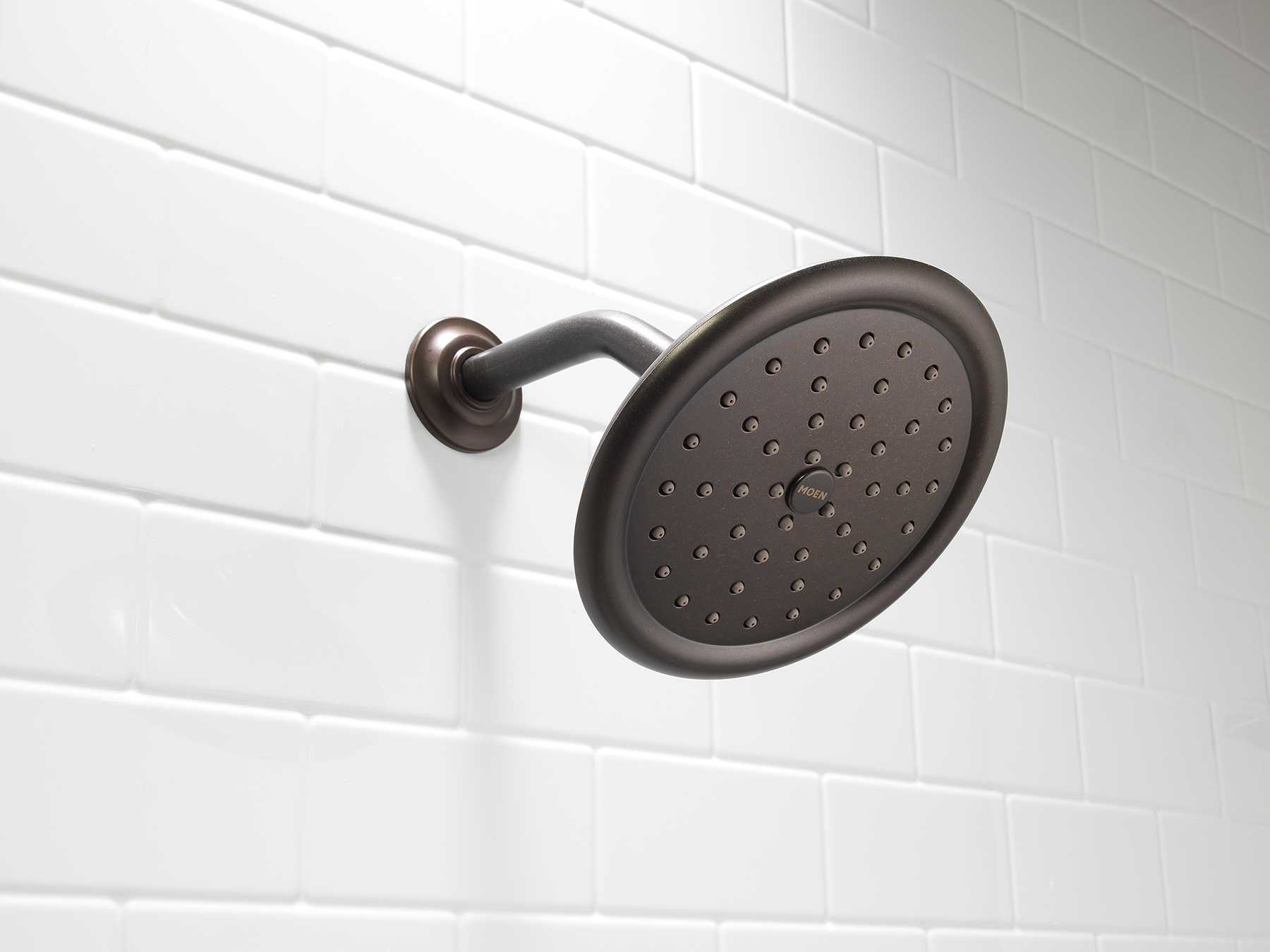 Bronze circular showerhead mounted on a curved arm against a white tiled bathroom wall.